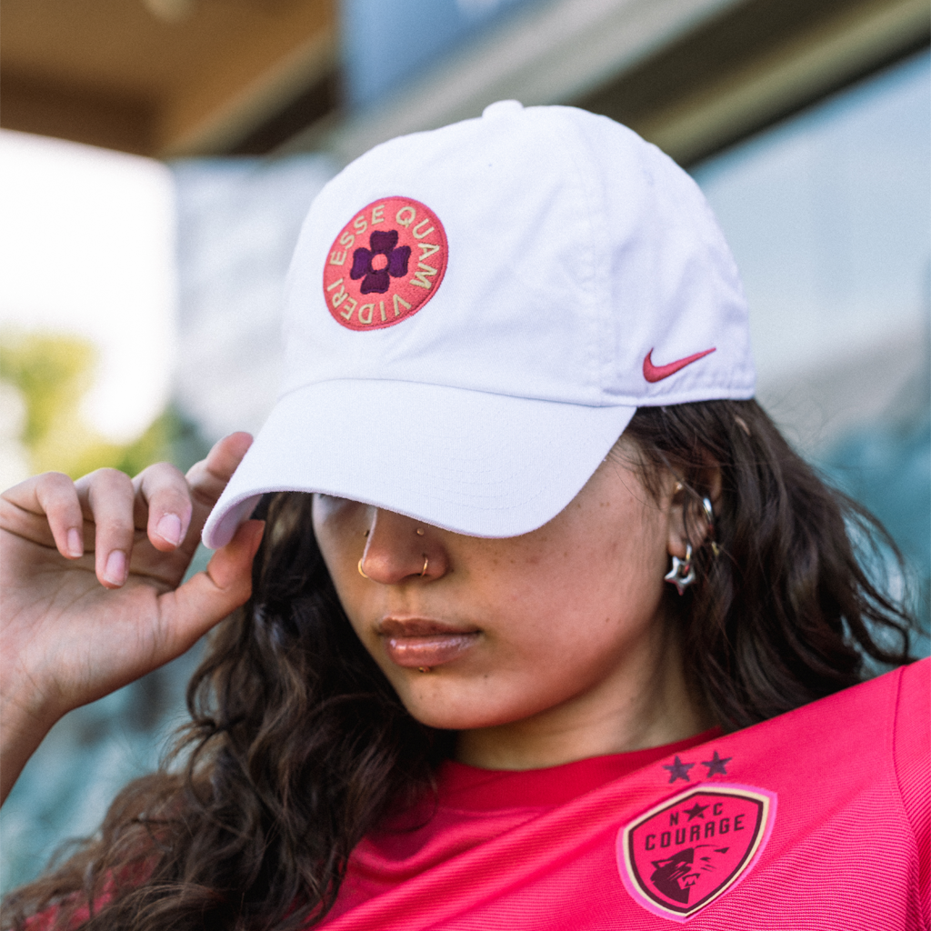 Person wearing a white cap with pink ESSE QUAM VIDERI logo and Nike logo