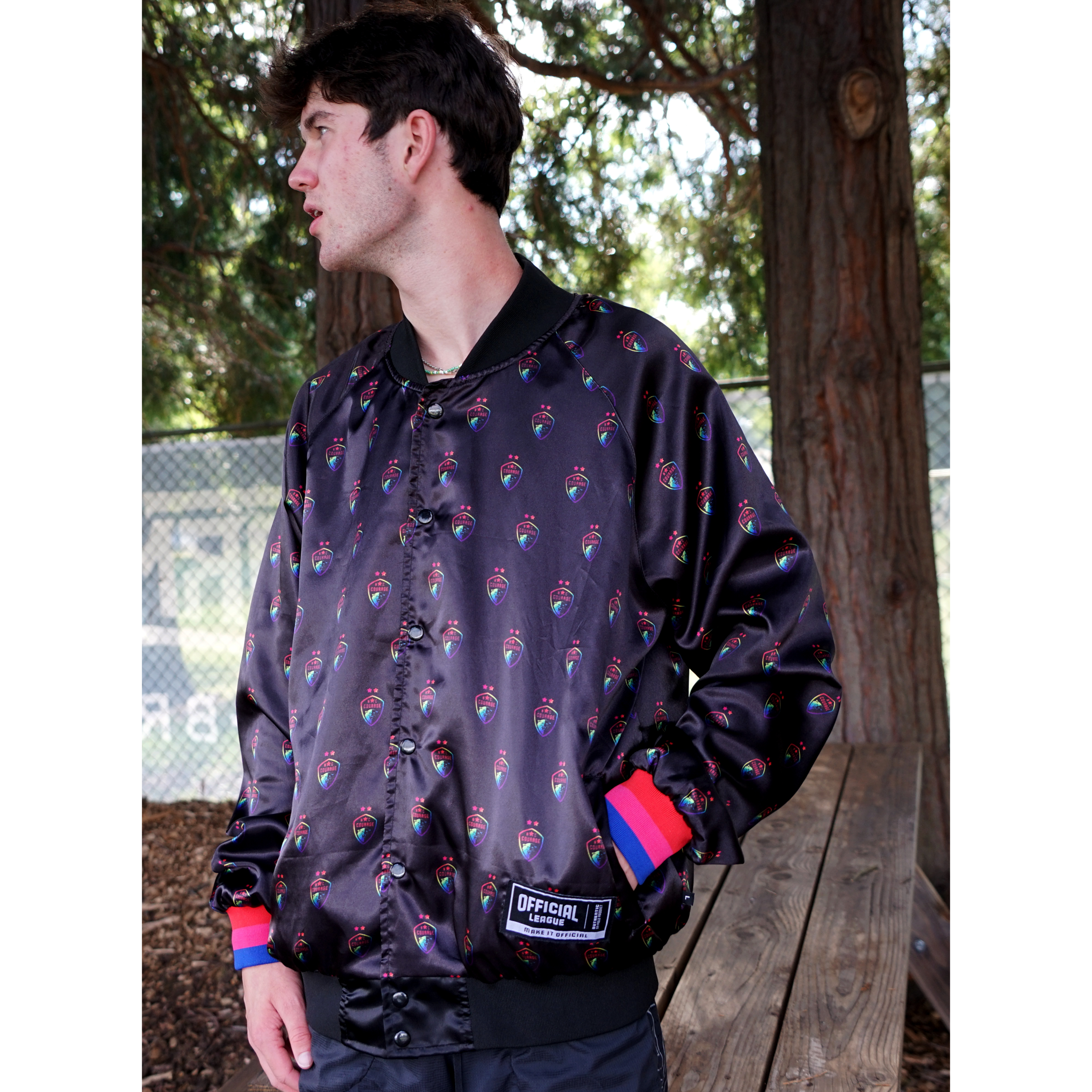 A man models a black satin jacket with the Courage pride logo covering the jacket.