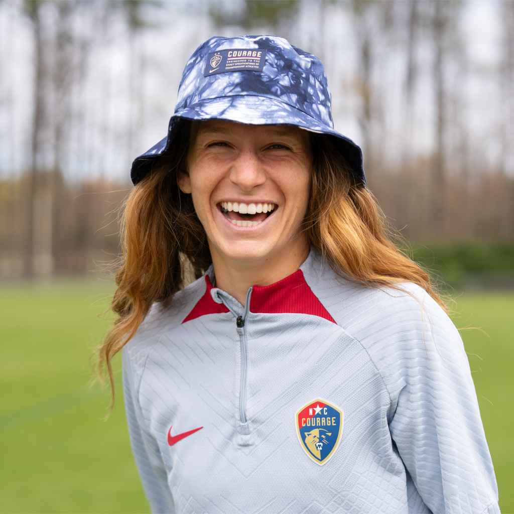 Ryan Williams models a tie-dye bucket hat with the NC Courage crest and a label that reads ' COURAGE TRUSTED TO THE CHAMPIONSHIP ATHLETES'.