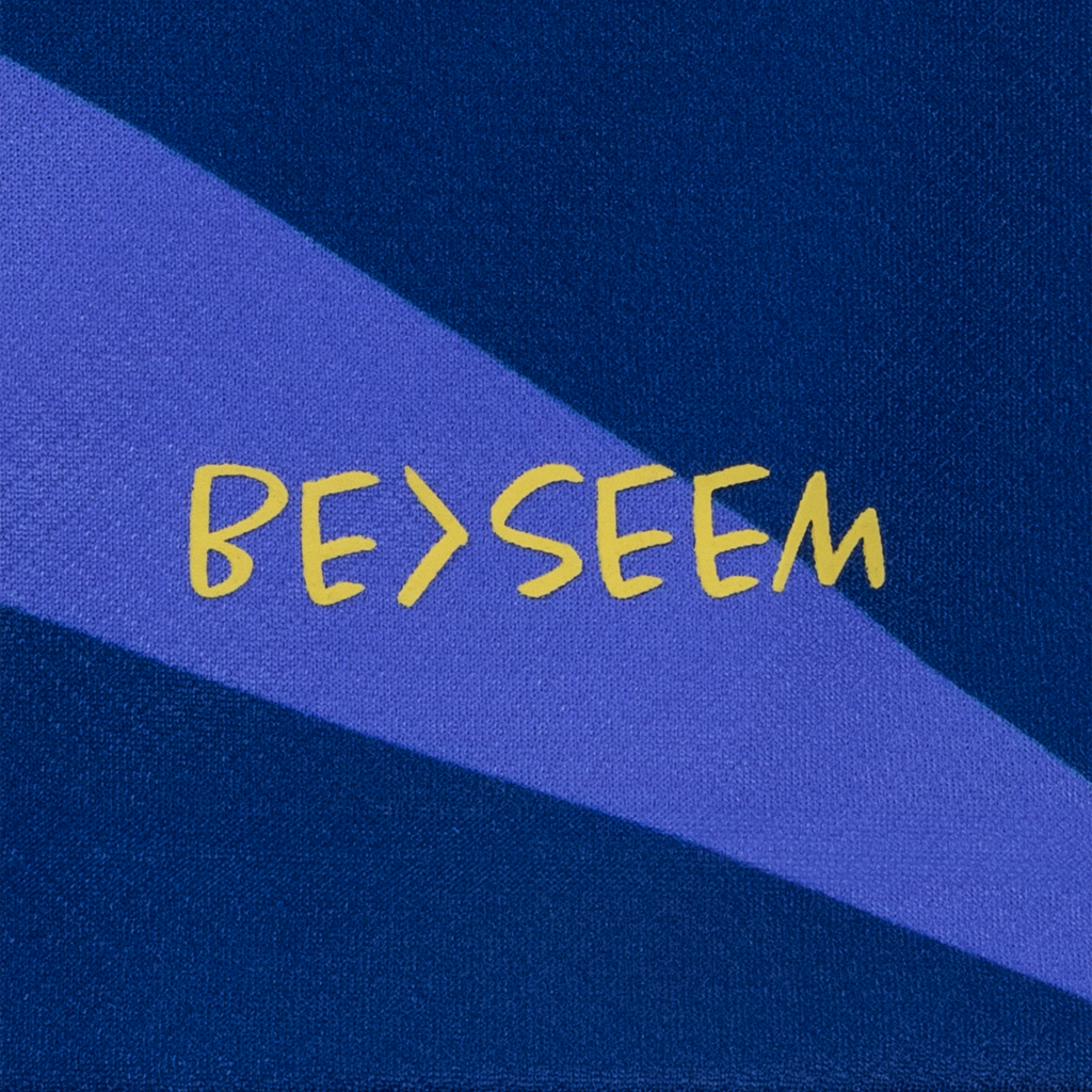 "Be>Seem" in gold on blue kit