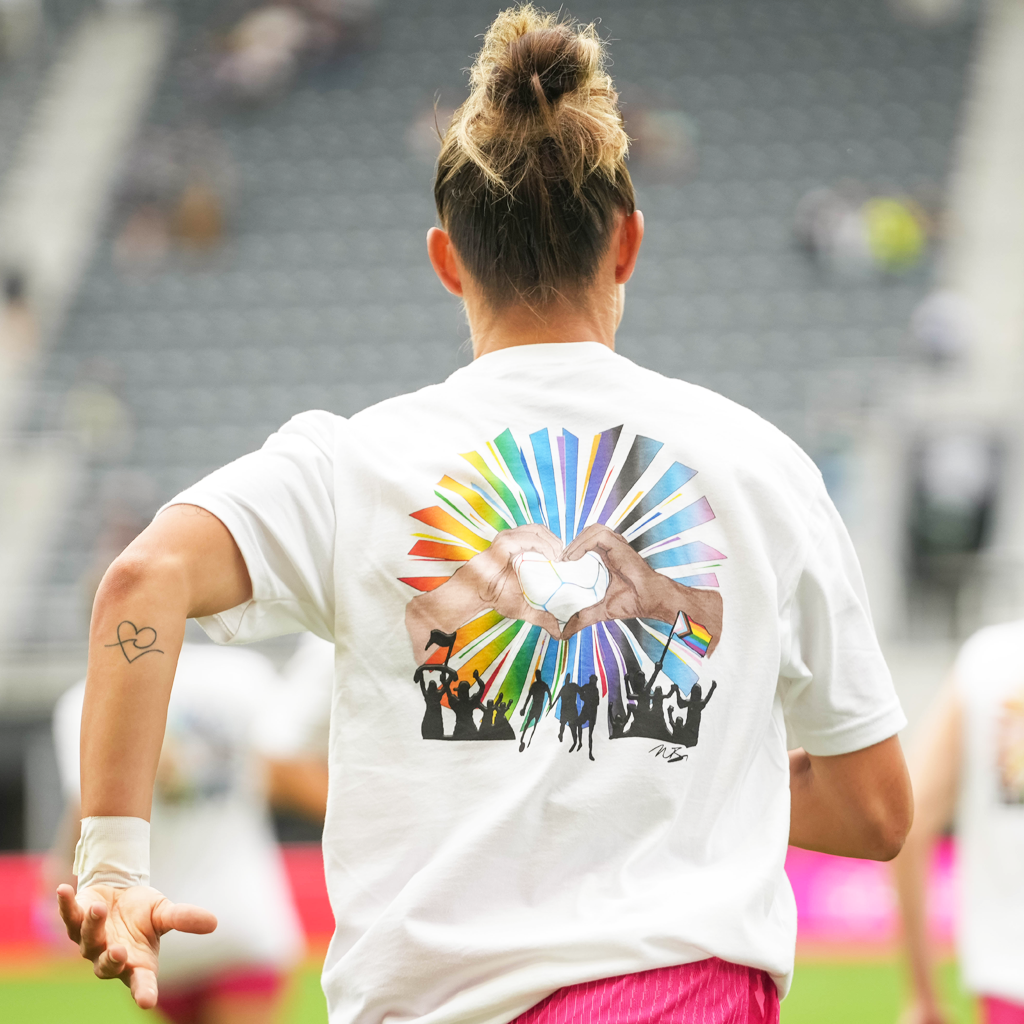 Player wearing the t shirt from the back. Back of the t-shirt shows hands making a heart with a rainbow of shapes
