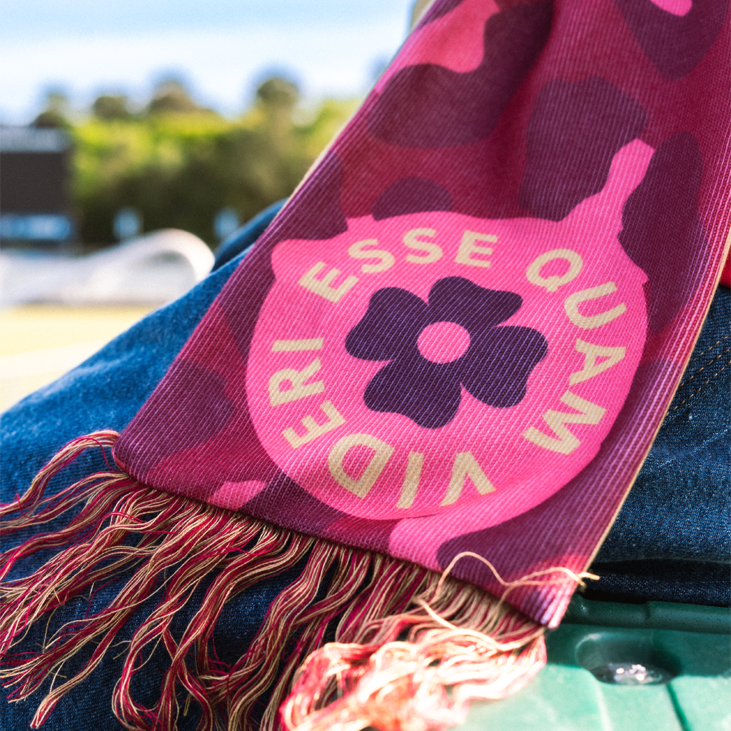 Pink scarf with floral design and text "Esse Quam Videri" draped over a person outdoors.