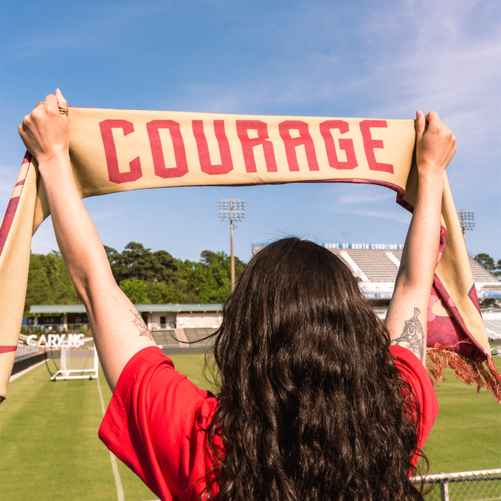Person holding a 'COURAGE' scarf on field