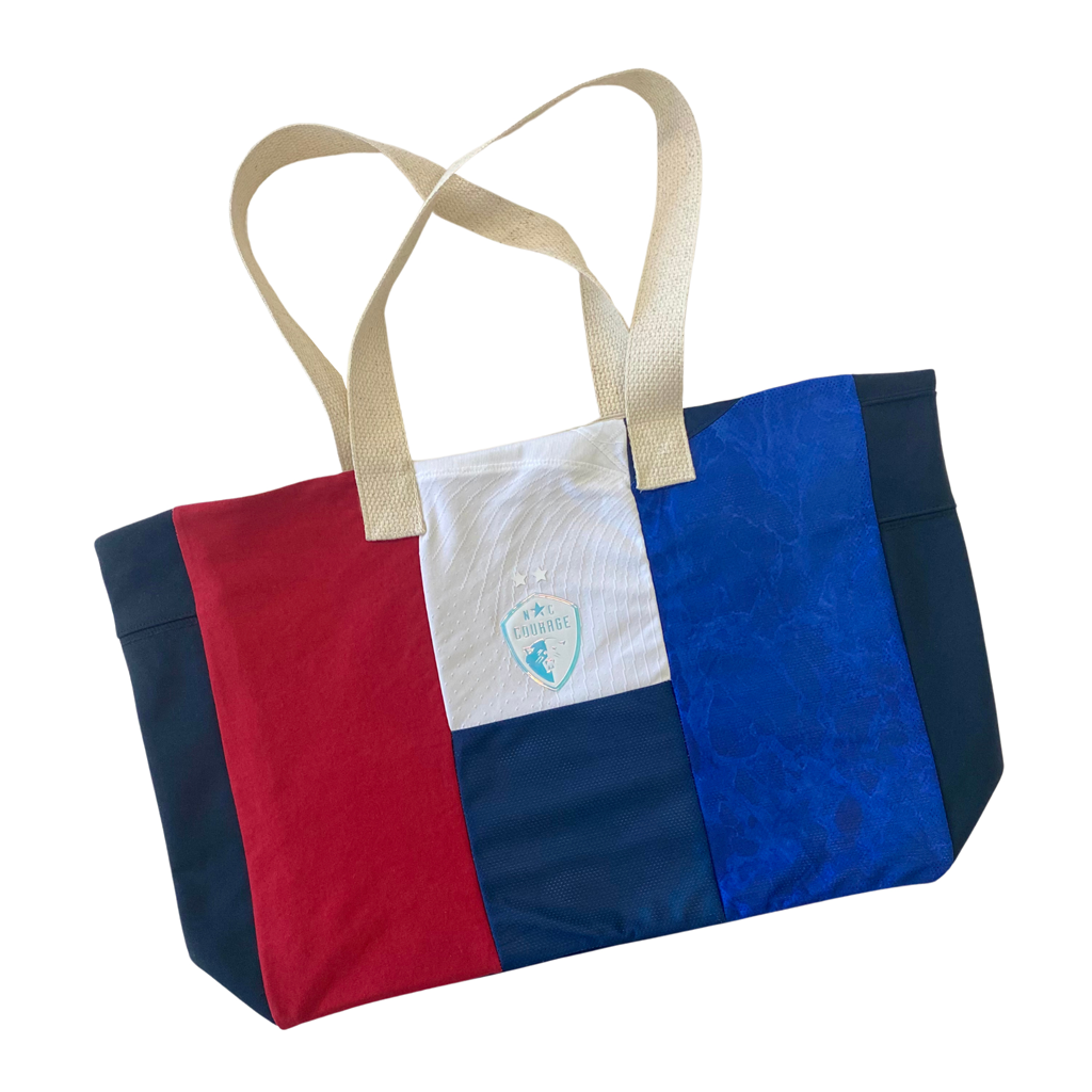 A beach bag with horizontal stripes in various colors, including blue, white, and red, with the NC Courage logo on the front.