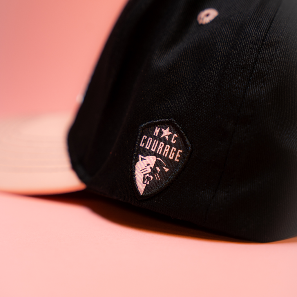 Black cap with a pink North Carolina Courage logo on a pink background