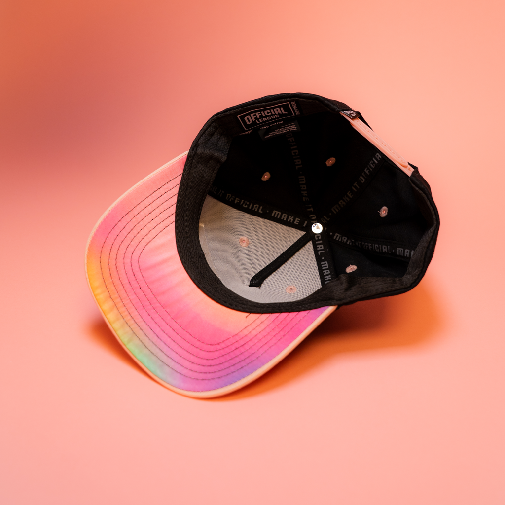 Black cap with rainbow brim on a pink gradient background