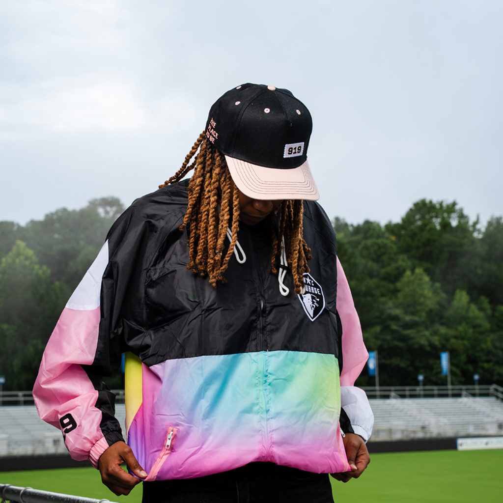 Person wearing a colorful jacket and black cap with a logo, standing outdoors.