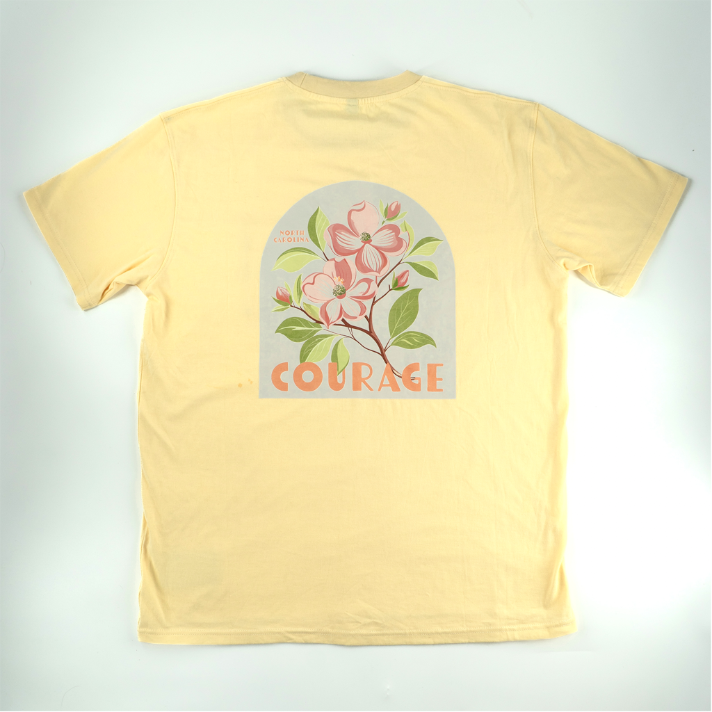 Back of yellow t-shirt with a white arch shaped filled with pink dogwood flowers and Courage underneath
