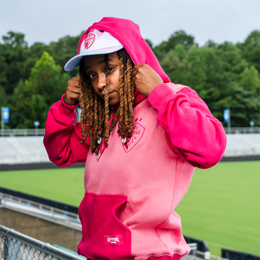 Model wearing pink hoodie with hood up over hat in the stadium