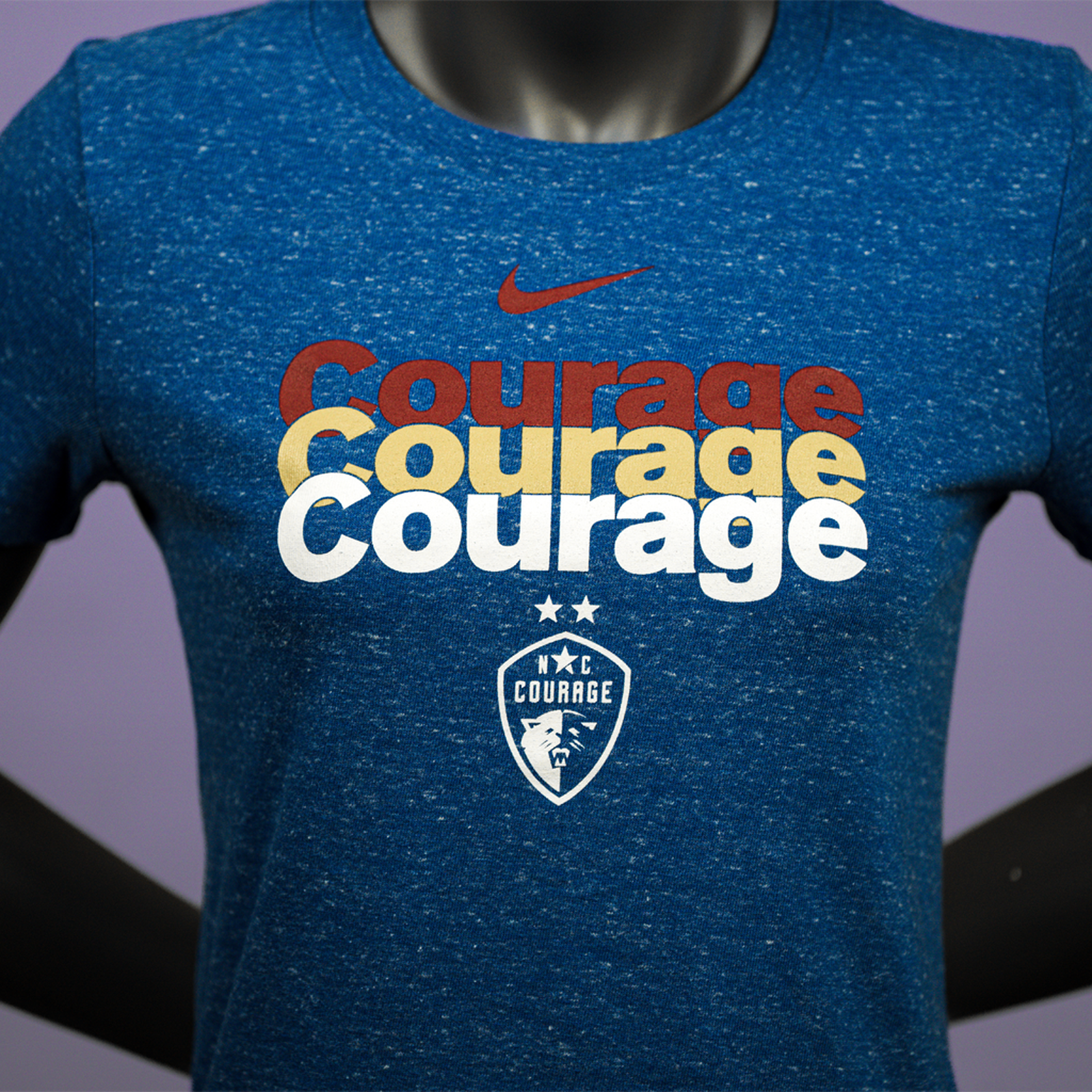 A close up of a mannequin wearing a royal blue t-shirt with a repeating pattern of the NC Courage logo in white, yellow, and red text.