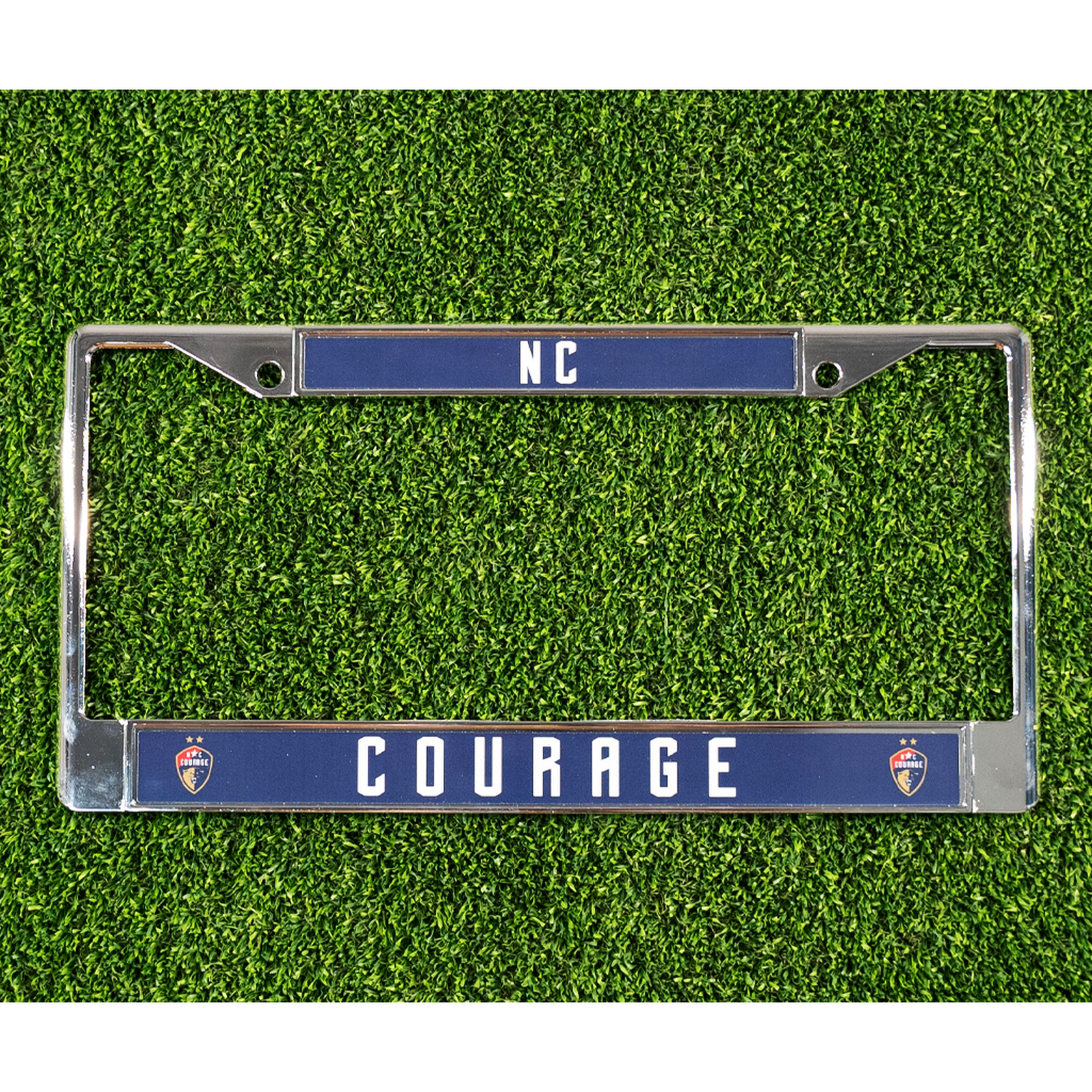 A chrome license plate frame with the NC Courage logo and the text 'NC' and 'COURAGE' on a artificial grass surface.
