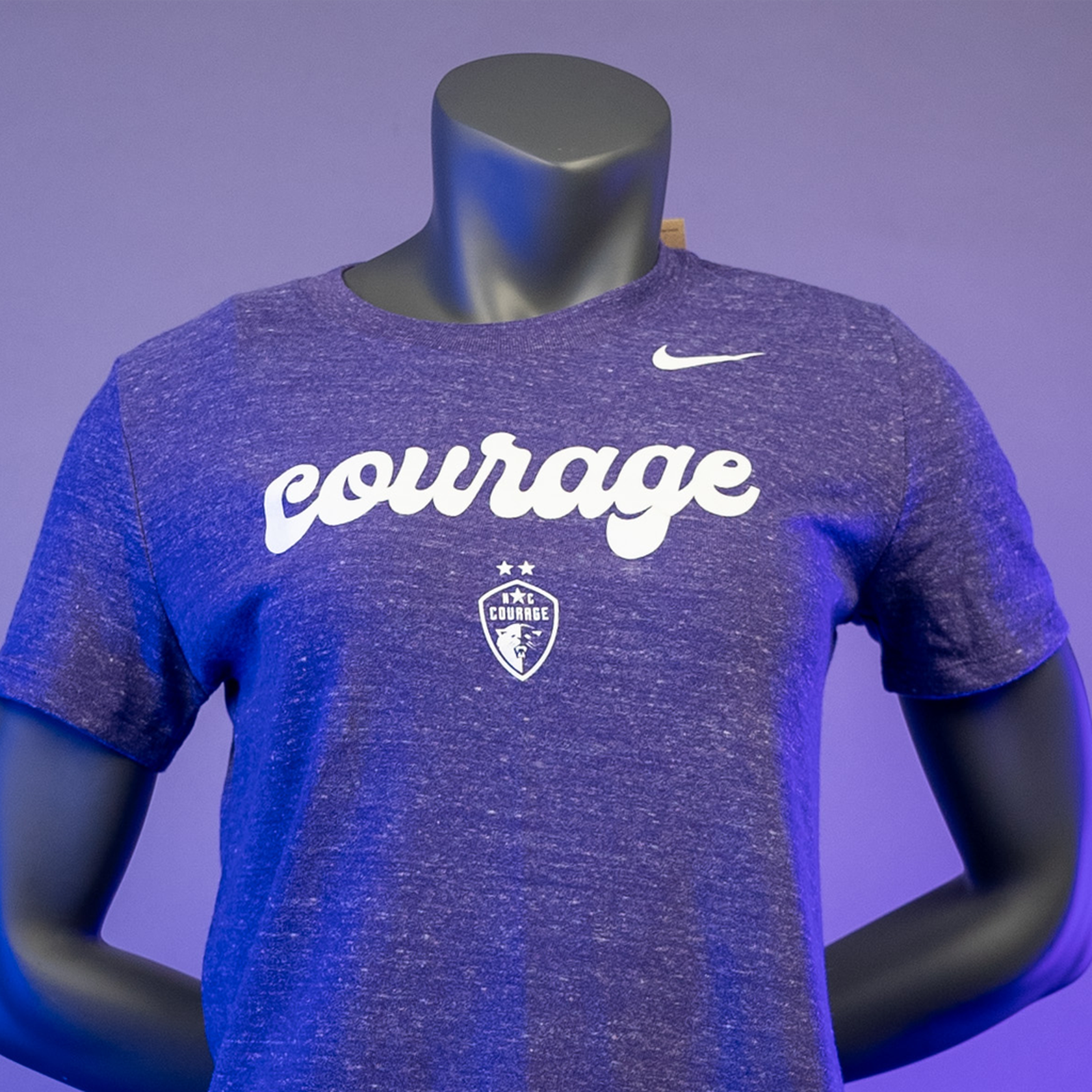 A close up of a mannequin wearing an orchid purple NC Courage women's varsity tee with the brand logo and the word 'courage' printed across the front.
