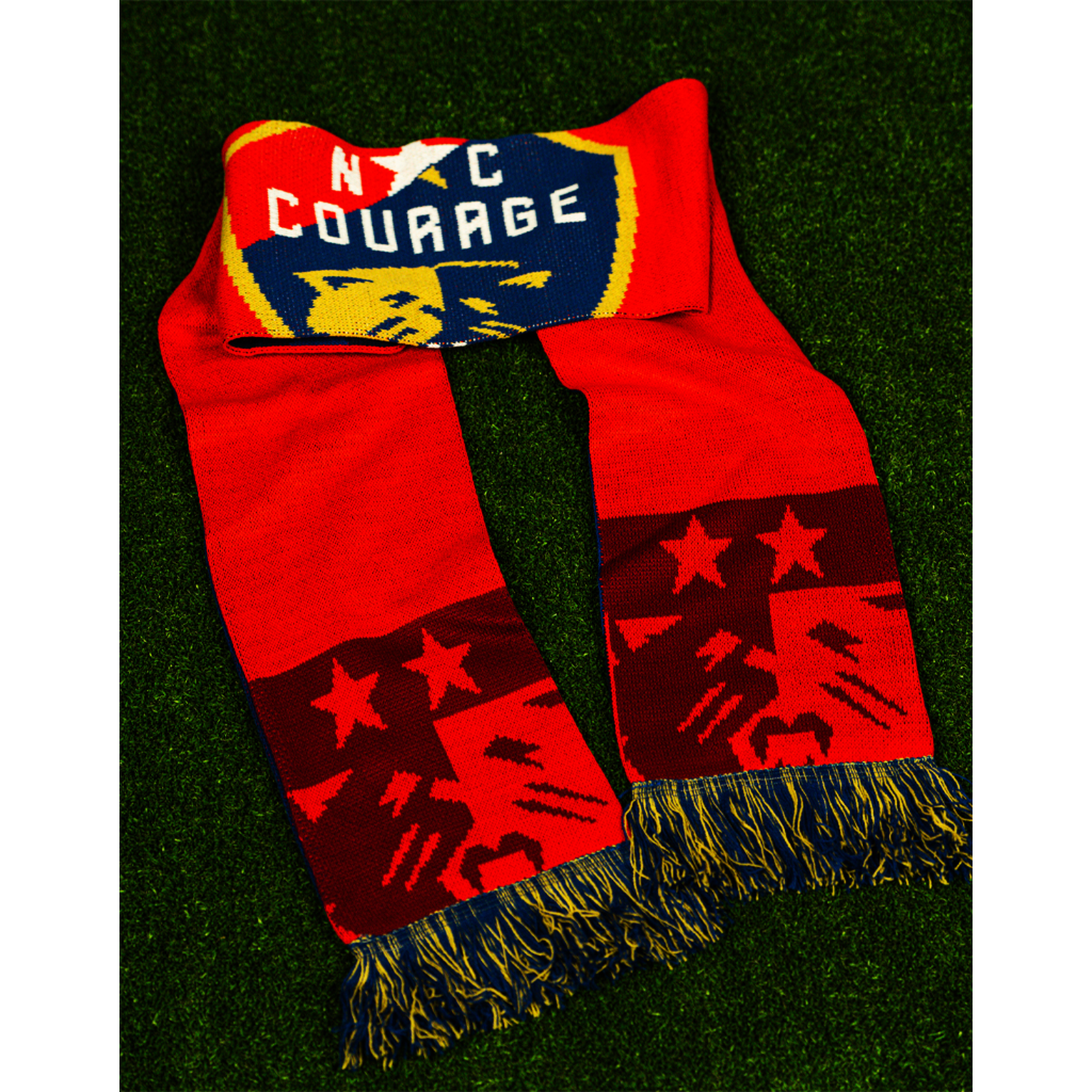 A red and blue knit scarf with 'NC Courage' text and a shield design, displayed on a grassy surface.