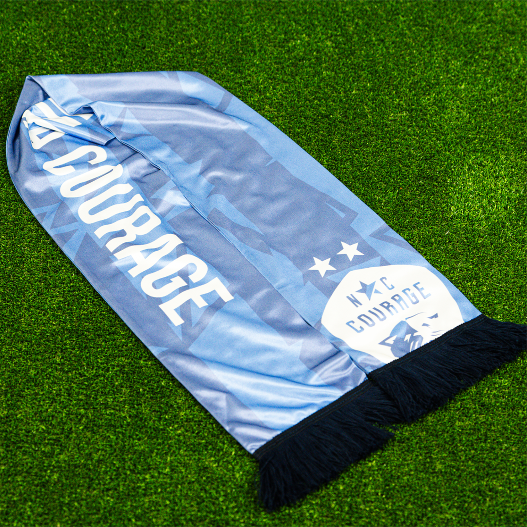 A purple scarf with the text 'ALL COURAGE' and the NC Courage logo, displayed on a green grass-like surface.