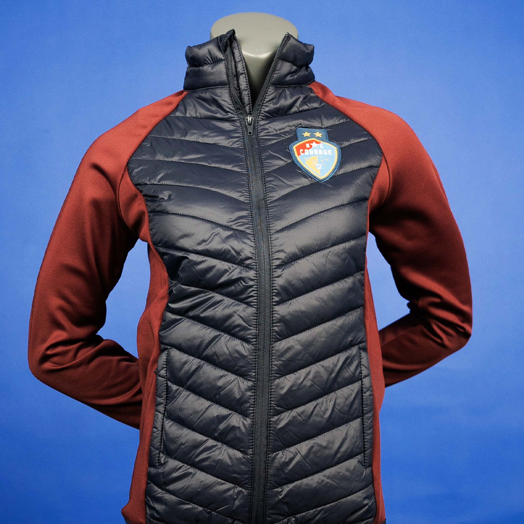 A woman's fit hybrid jacket featuring insulated panels and a stretchy fabric, primarily in black and red colors, with the NC Courage logo on the chest.
