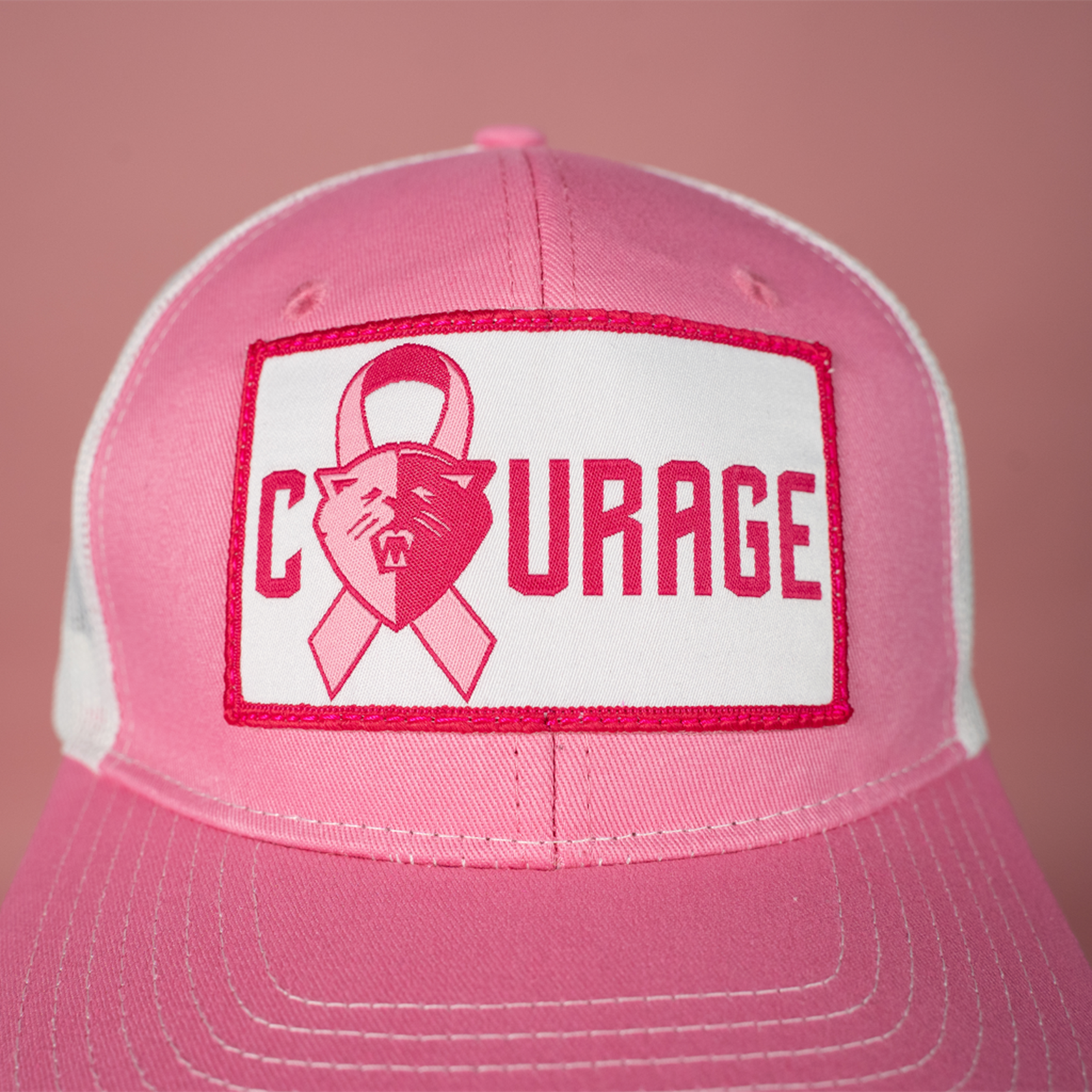Closeup of a pink and white trucker hat with the NC Courage logo and the word 'COURAGE' on a patch on the front.