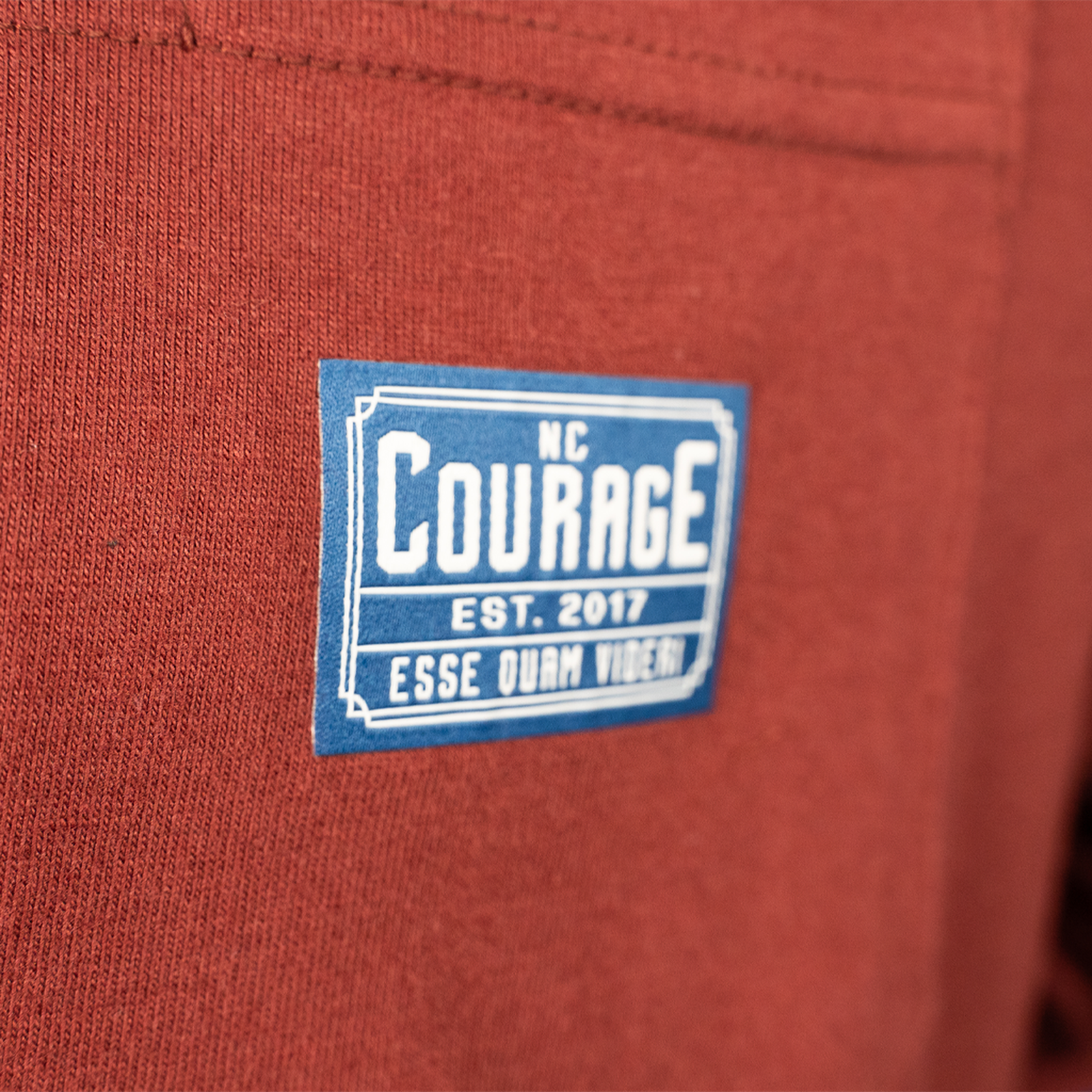 Close up of a Blue NC Courage Patch on a rust-colored long sleeve shirt