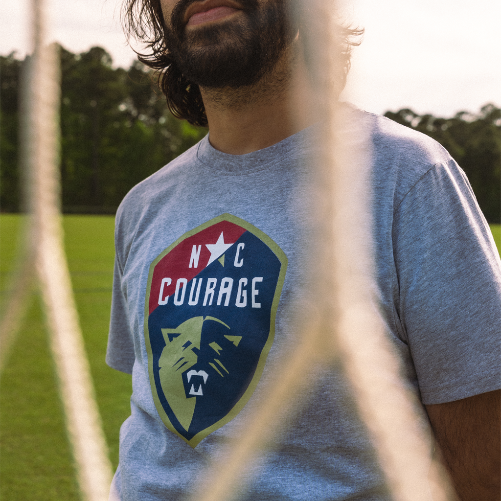 Person wearing a gray t-shirt with 'NC Courage' logo in an outdoor setting