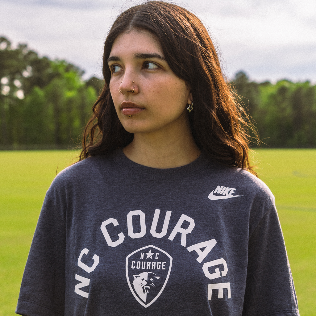 Person wearing Navy blue Nike t-shirt with 'NC Courage' text curving over North Carolina Courage logo outside.