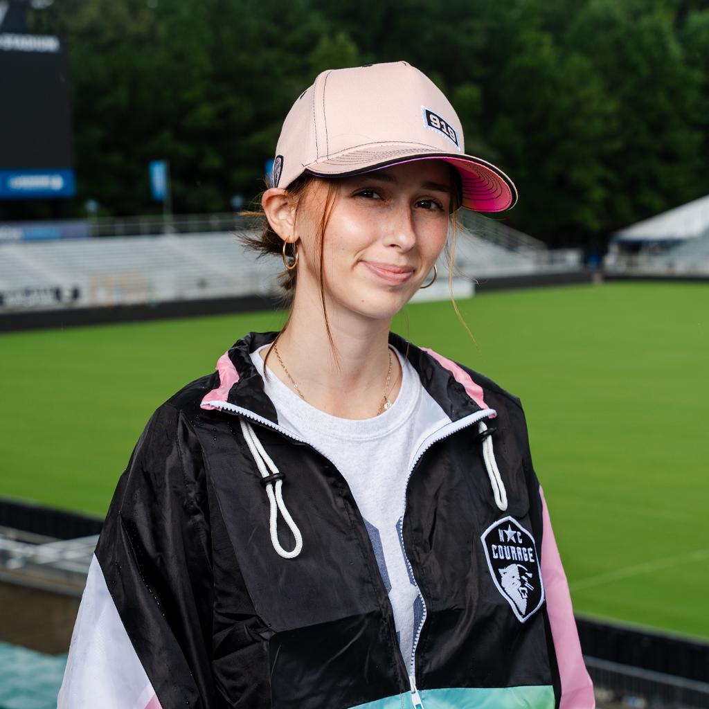 Person wearing a pink cap and jacket with branding on a sports field
