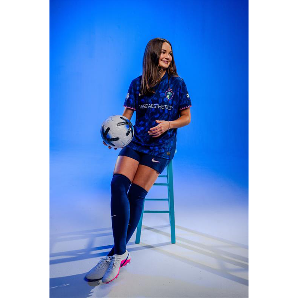 Woman in a blue sports jersey holding a soccer ball on a blue background