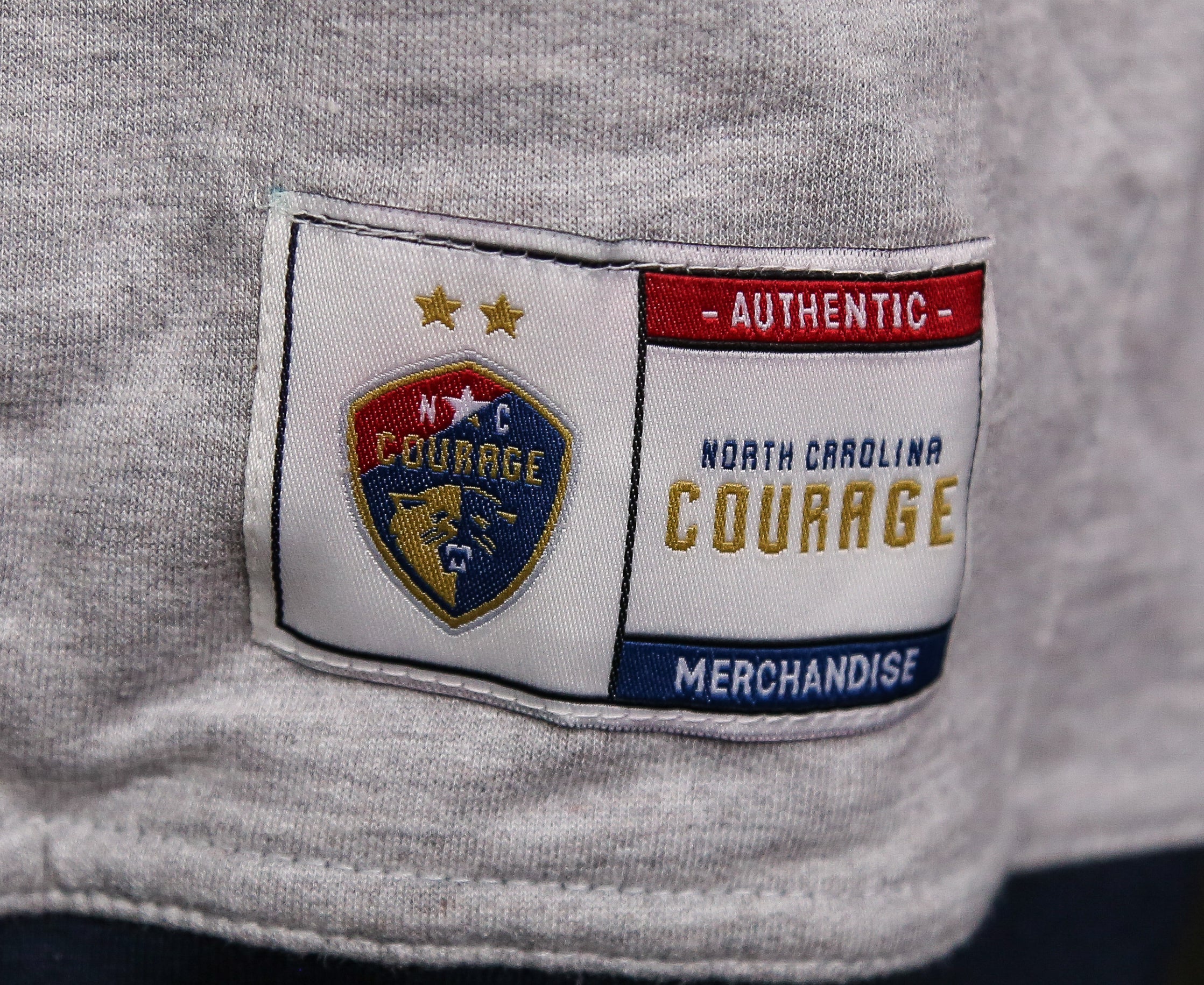 A gray hoodie with contrasting blue hood and cuffs, featuring the text 'NORTH CAROLINA COURAGE' on the front.