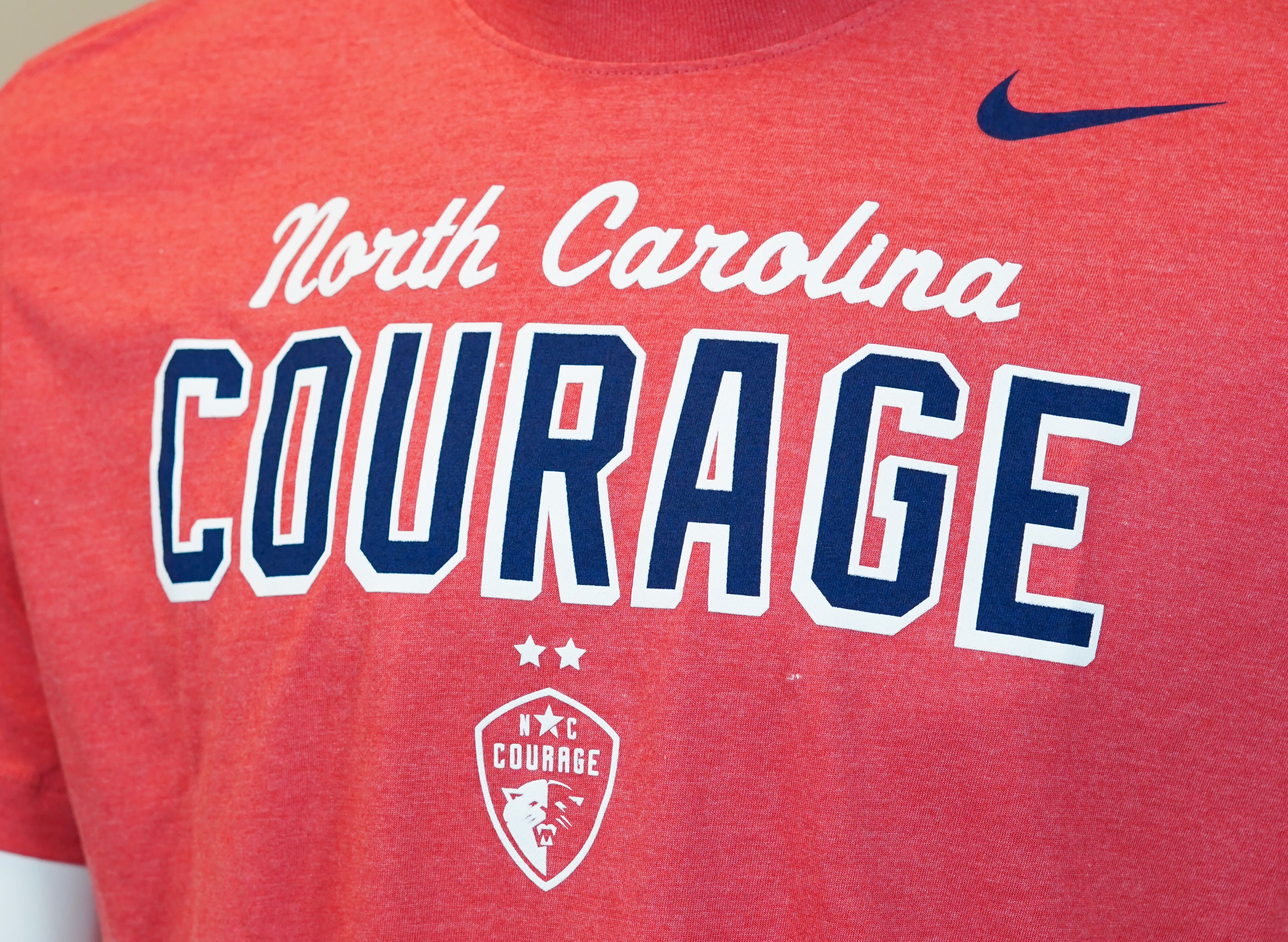 A red Nike t-shirt with 'North Carolina Courage' written in white and blue lettering, featuring the Nike logo.