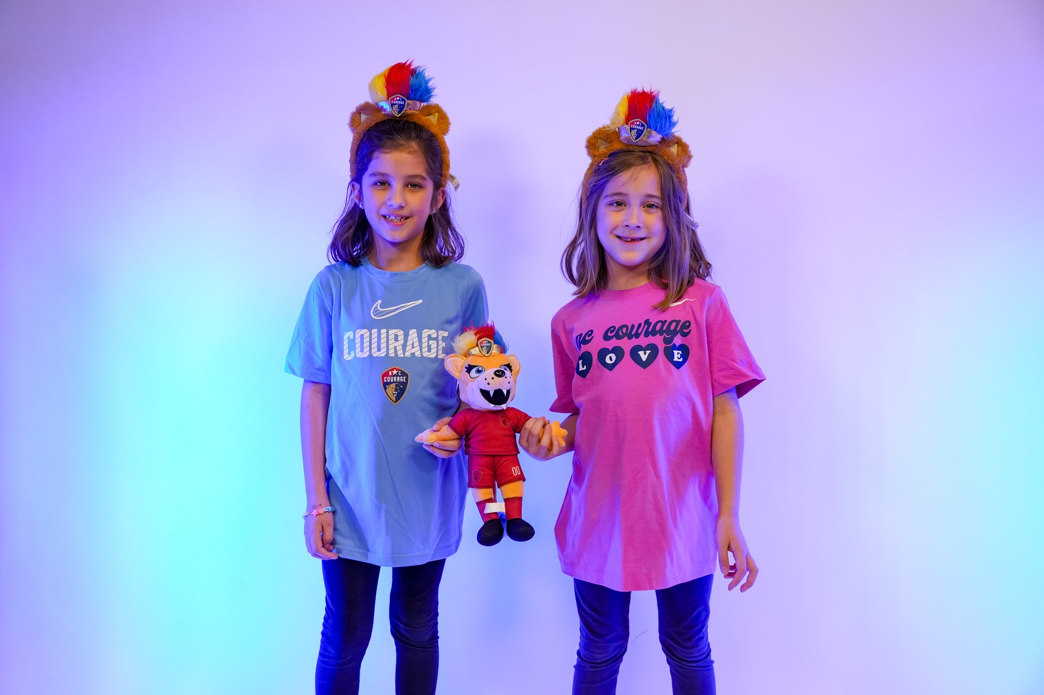 Two children wearing colorful headbands and holding plush toys against a gradient background