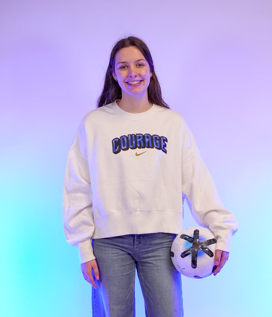 Person wearing a white Nike sweatshirt with Courage in blue in the center. 