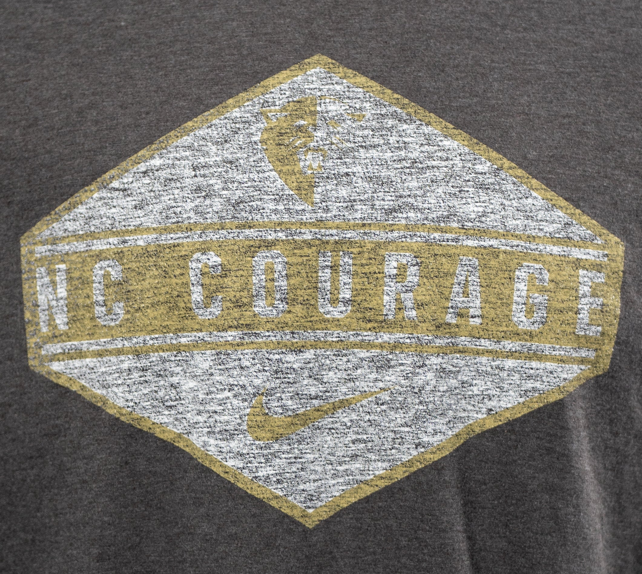 A black heathered t-shirt with a large diamond-shaped graphic on the front featuring the NC Courage logo, name, and Nike swoosh in gold, white, and grey colors.