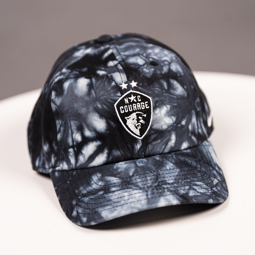 A black tie-dye baseball cap with the NC Courage logo embroidered on the front.