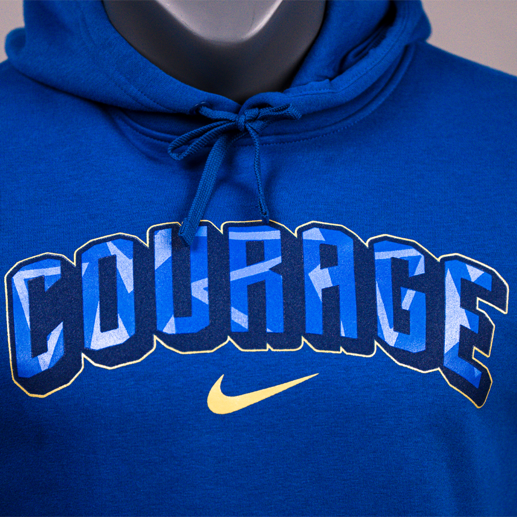 A closeup of a blue hoodie with the text 'COURAGE' arched across the front, featuring the Nike logo.