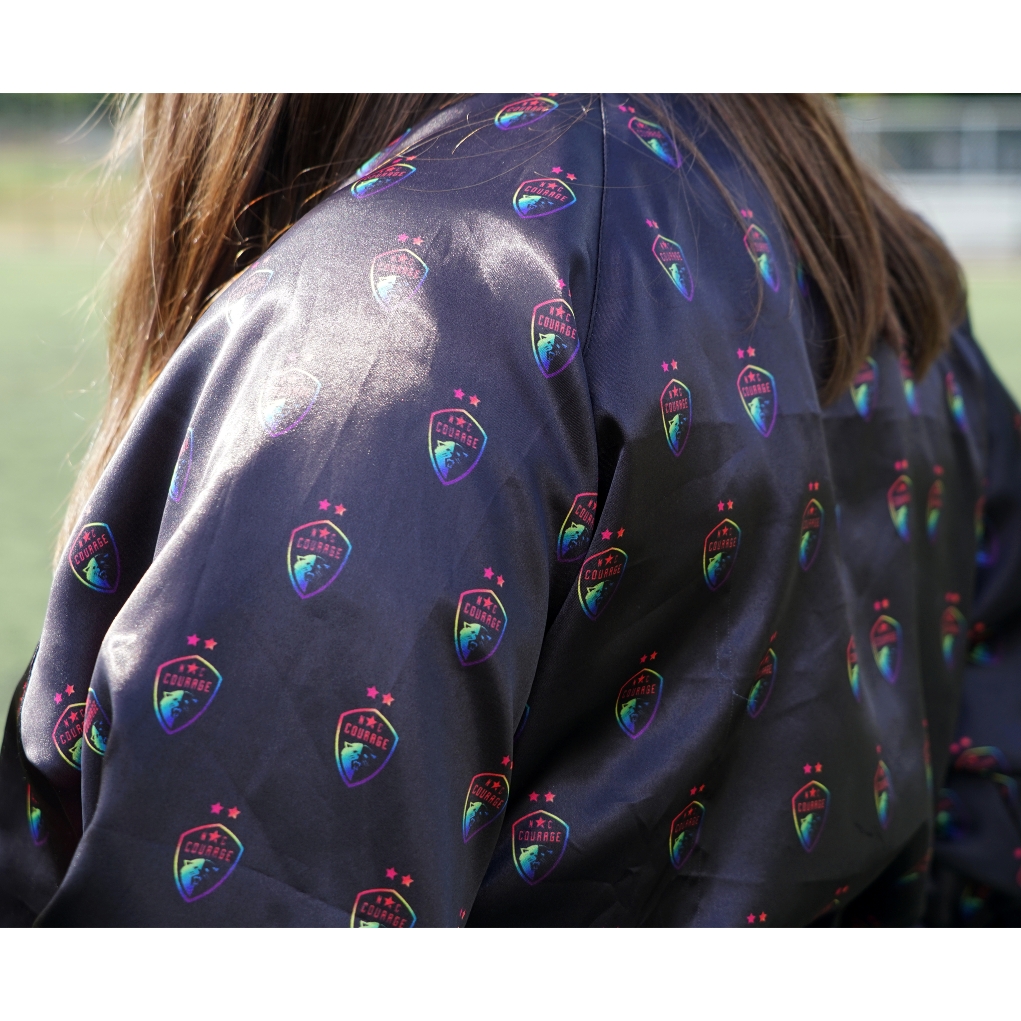 A closeup of a woman wearing a black satin jacket with the pride logo all over the jacket.