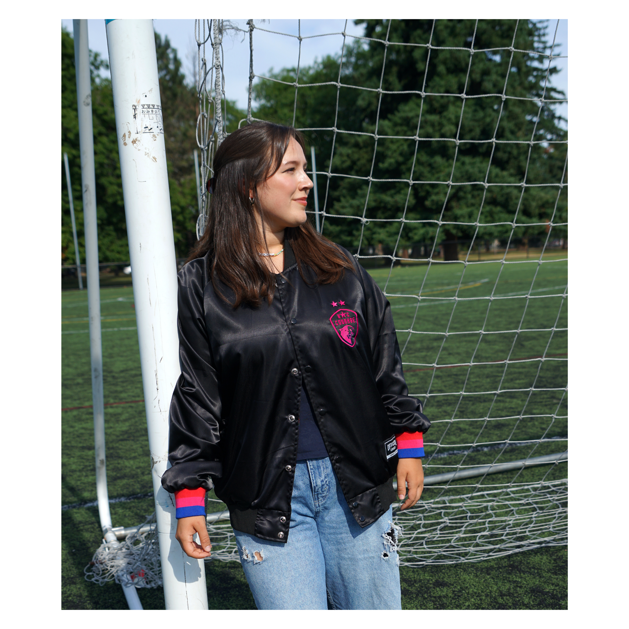 A person wearing a black satin jacket with red and blue trim and embroidered details, standing next to a soccer goal.