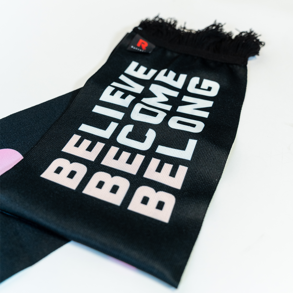 Closeup of black scarf that says Believe Become Belong in pastel pink and blue. 
