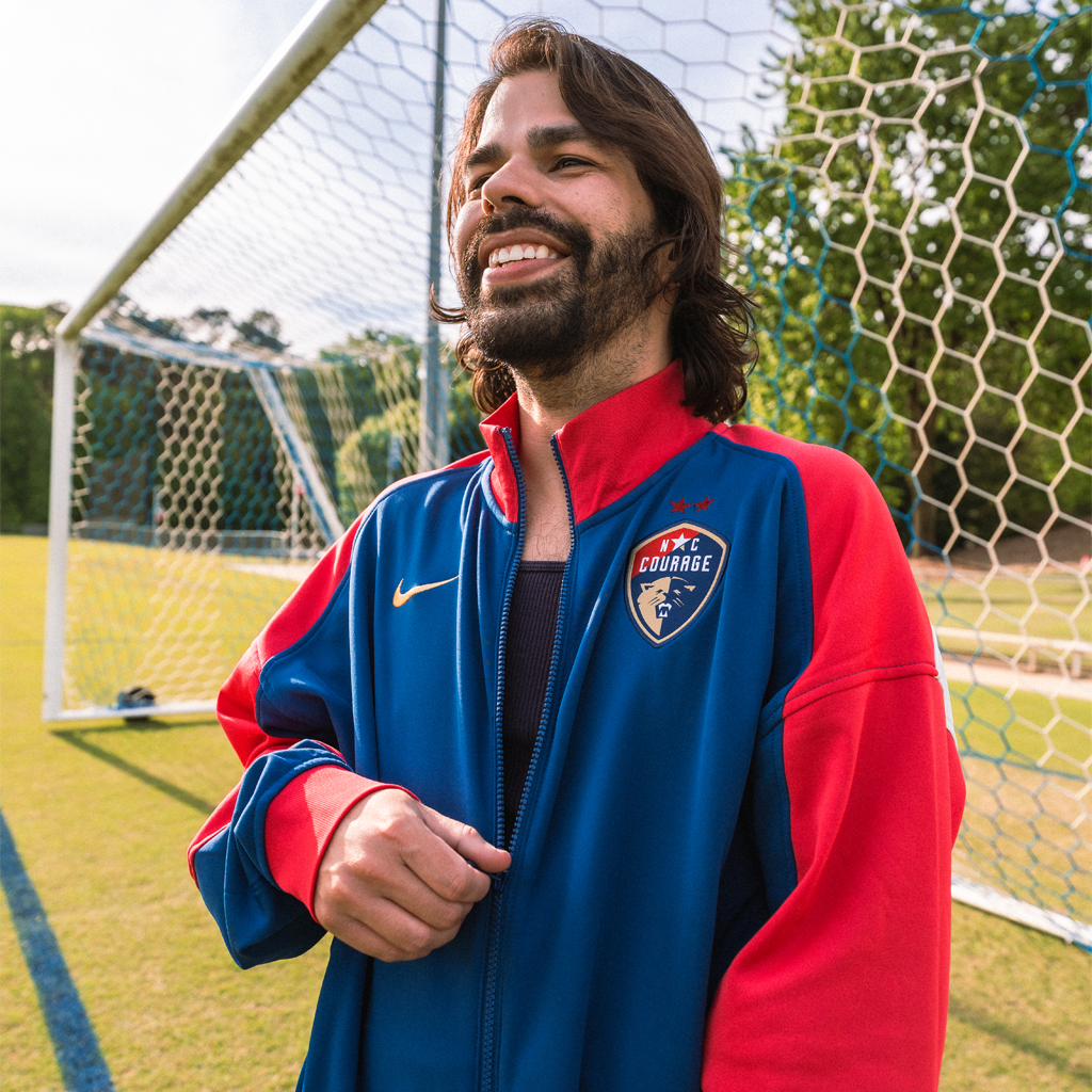 Person wearing a sports jacket with red and blue color blocks, featuring a zipper, Nike logo on the left, and the North Carolina logo on the right. 