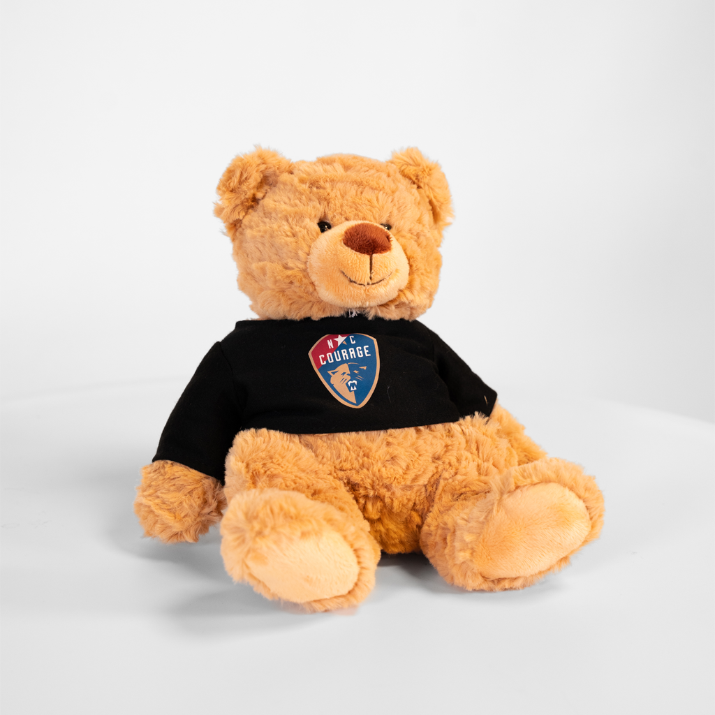 Four plush toy animals, including a bear, a pink pig, a wolf, and a dog, each wearing a black shirt with a logo, seated in a row on a white surface against a neutral background.