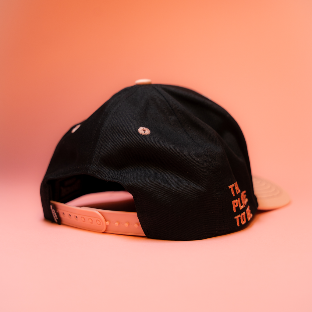Black cap with pink text on a peach background