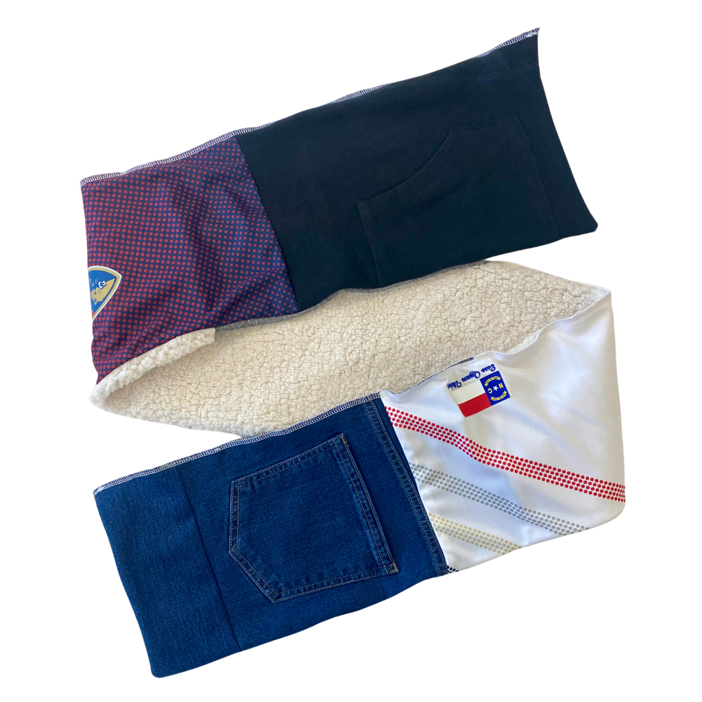 A scarf with integrated pockets, featuring a variety of fabrics and colors, including blue denim and a white patterned section.