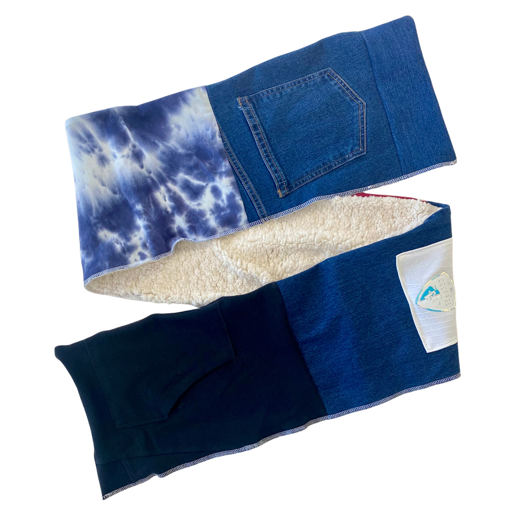 A scarf with integrated pockets, featuring a variety of fabrics and colors, including blue denim and a white patterned section.