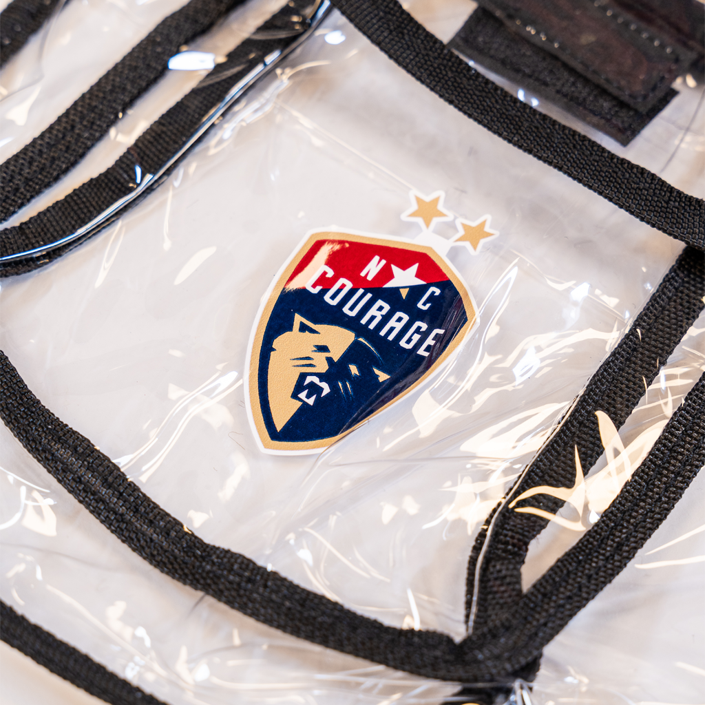 Closeup of clear bag with black straps featuring the North Carolina Courage logo and text on a white background