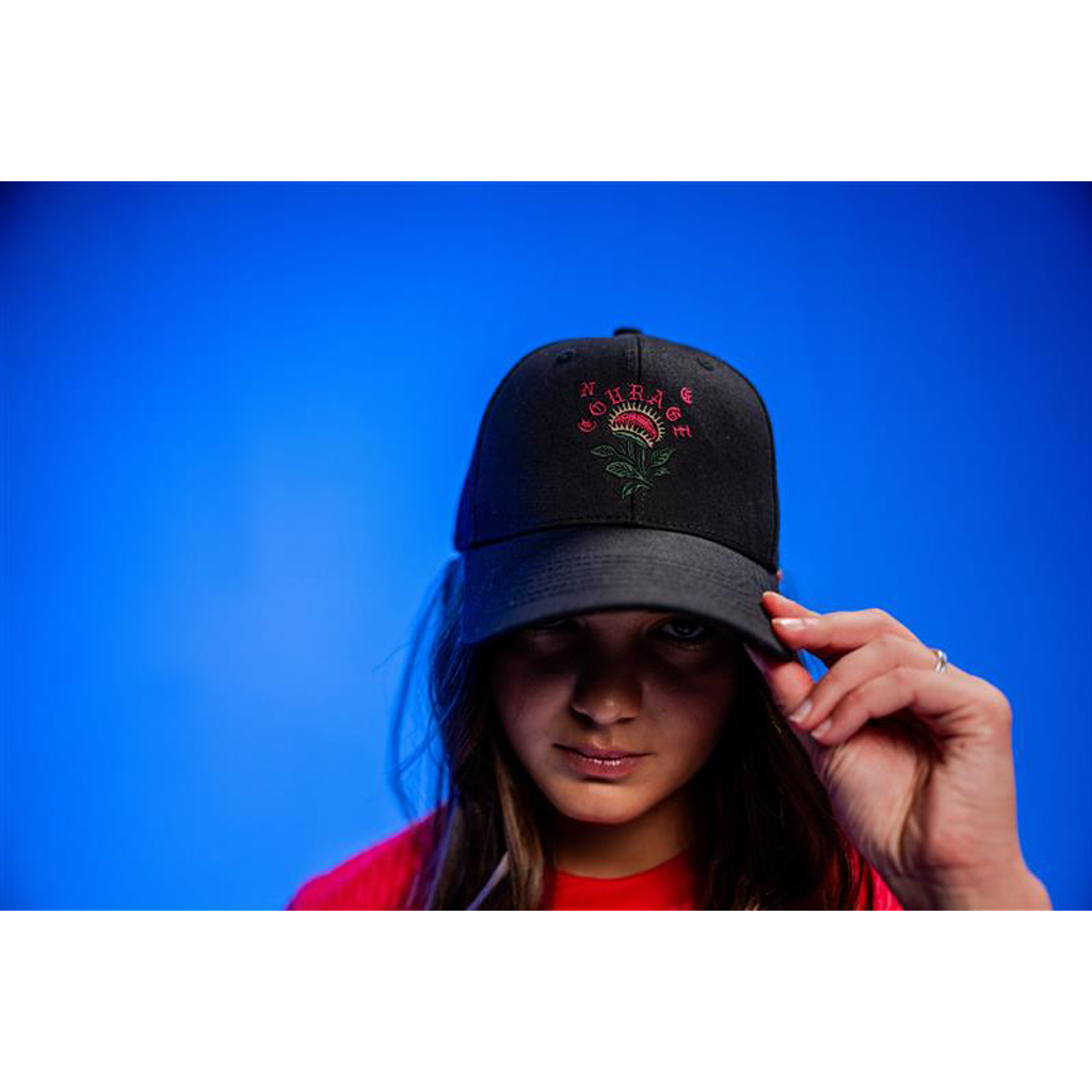 Person wearing a black cap with a logo against a blue background