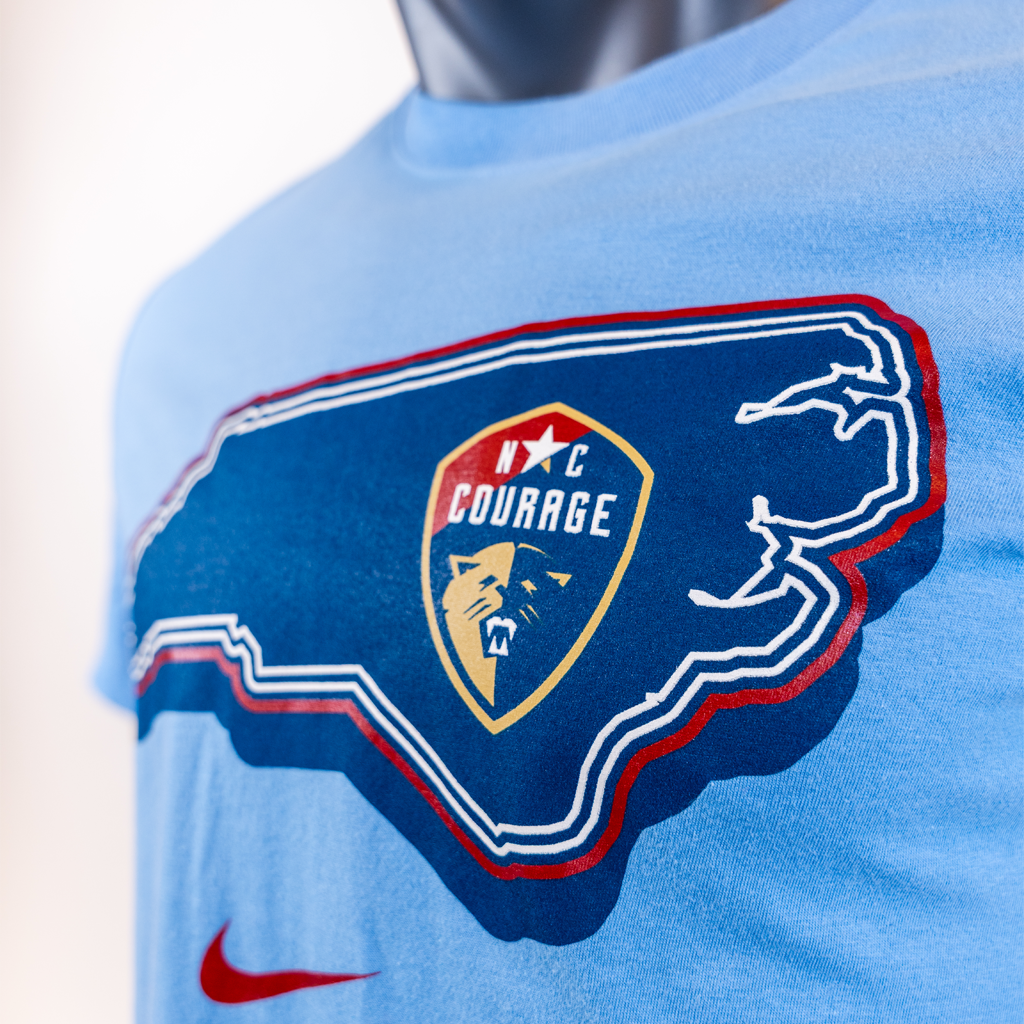 Light blue NC Courage Home State Tee with a logo of a state outline and 'NC Courage' logo on a mannequin.