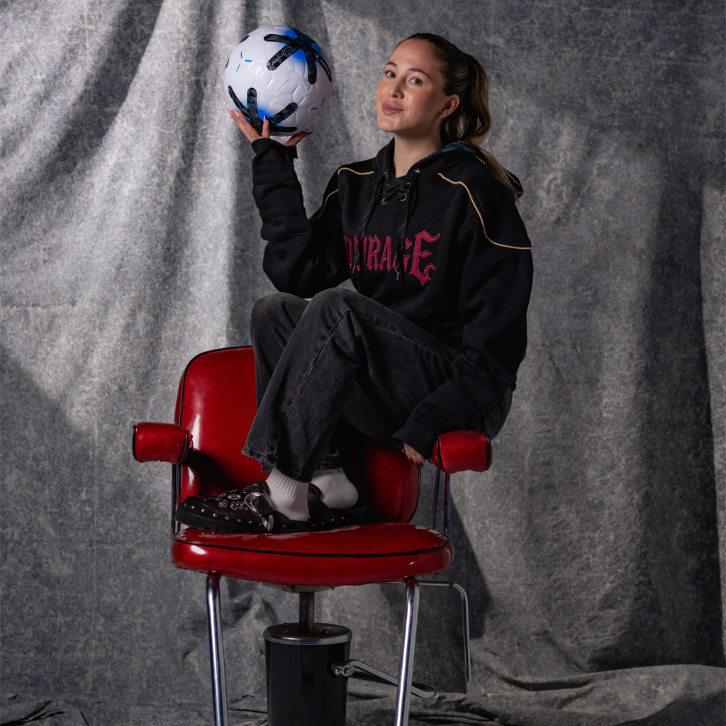 Person sitting on a red chair holding a soccer ball against a gray background