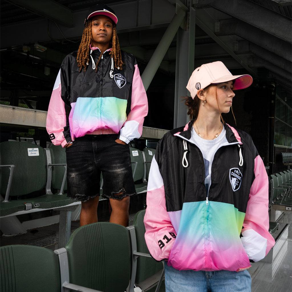 Two people wearing colorful "The Place to Be" Chute Jacket in a stadium setting