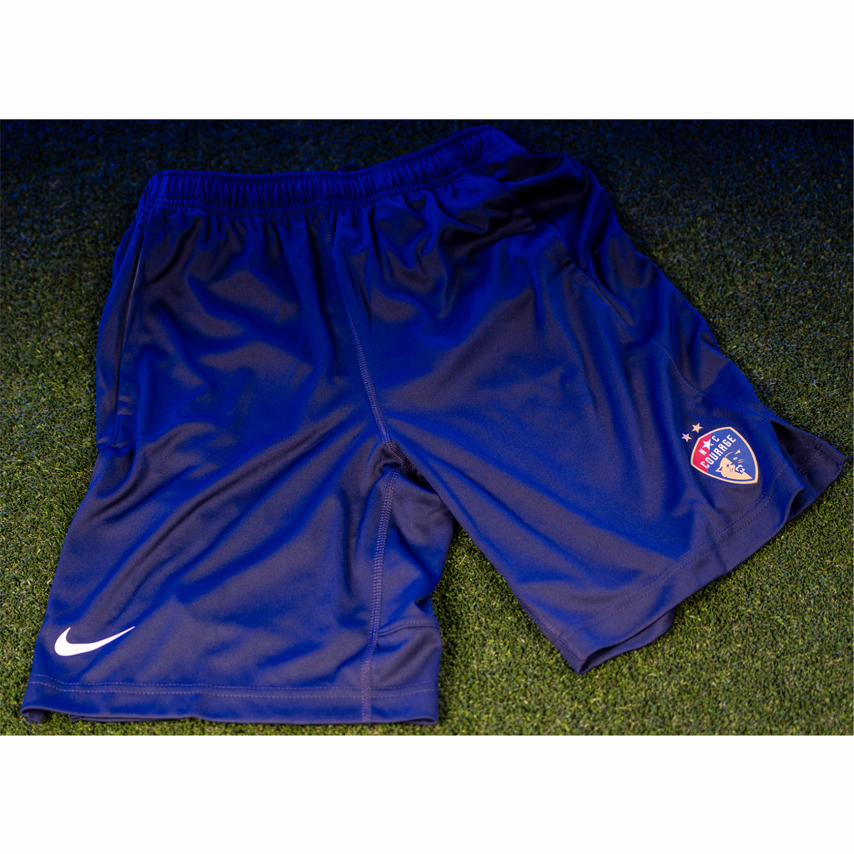 A pair of blue sports shorts with a logo on the left leg and a small white Nike logo on the lower right corner.