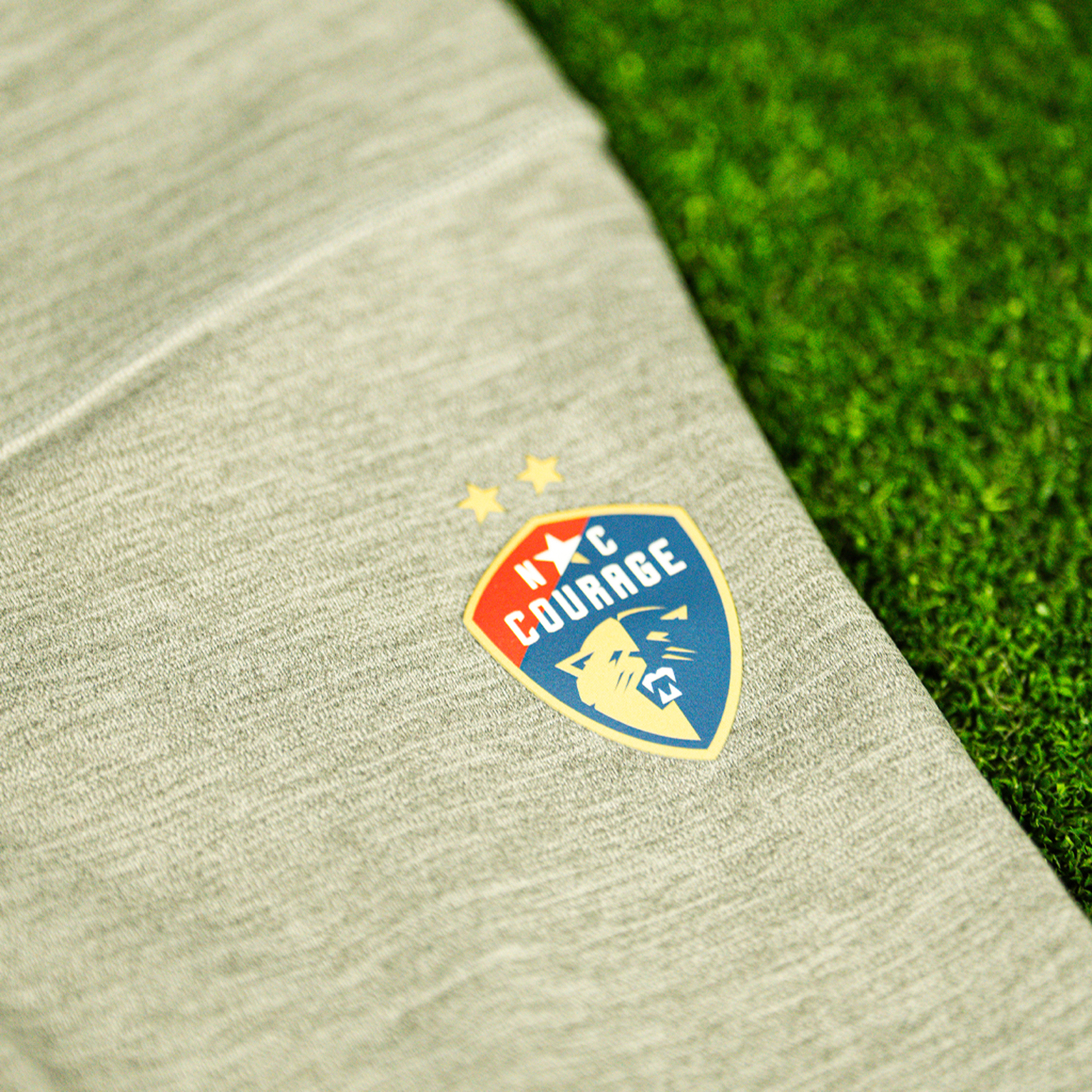 A close up of a pair of gray Nike Dri-FIT leggings with the NC Courage logo on the front, displayed on a green artificial turf surface.