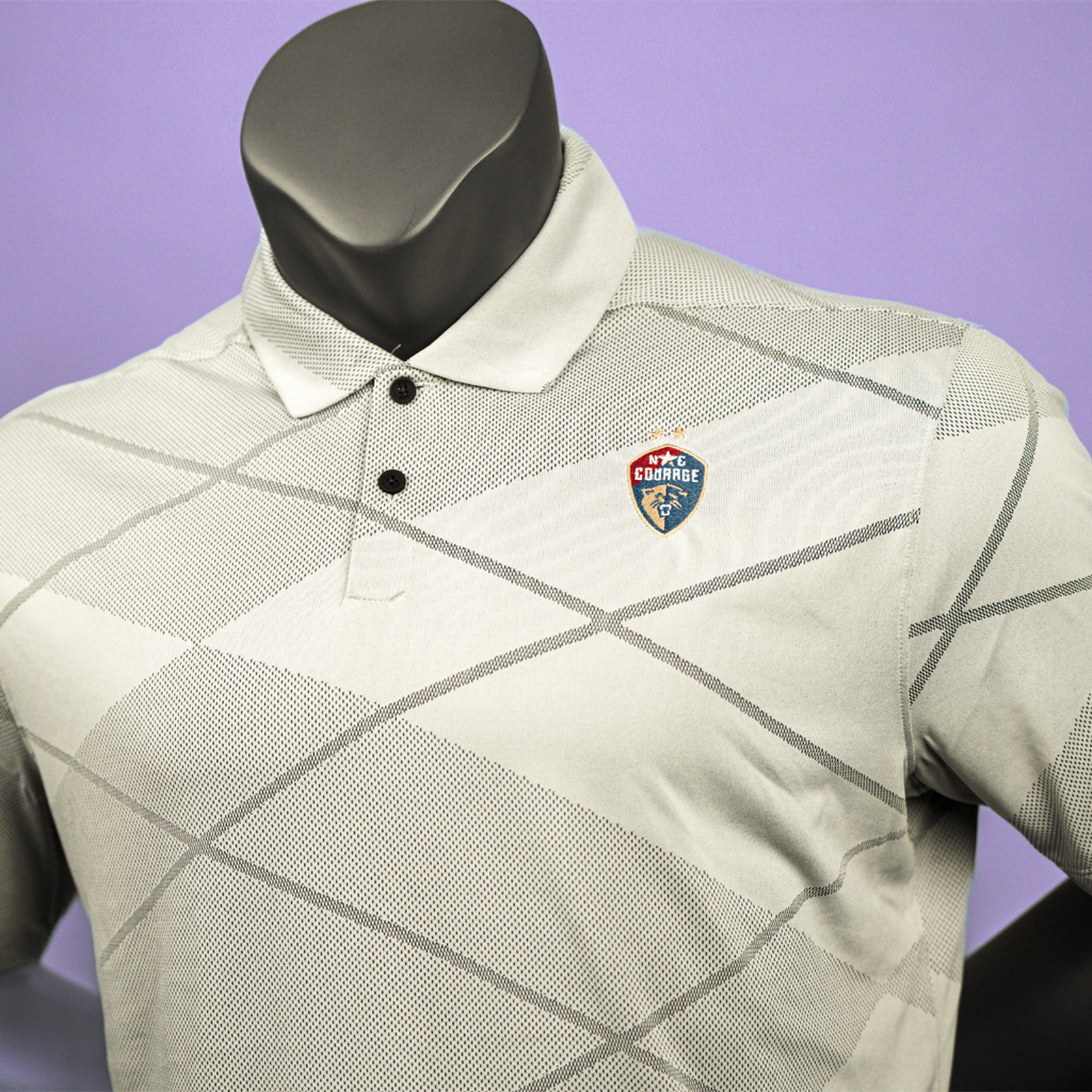 A close up of a gray jacquard pattern polo shirt with the NC Courage logo embroidered on the chest displayed on a mannequin.