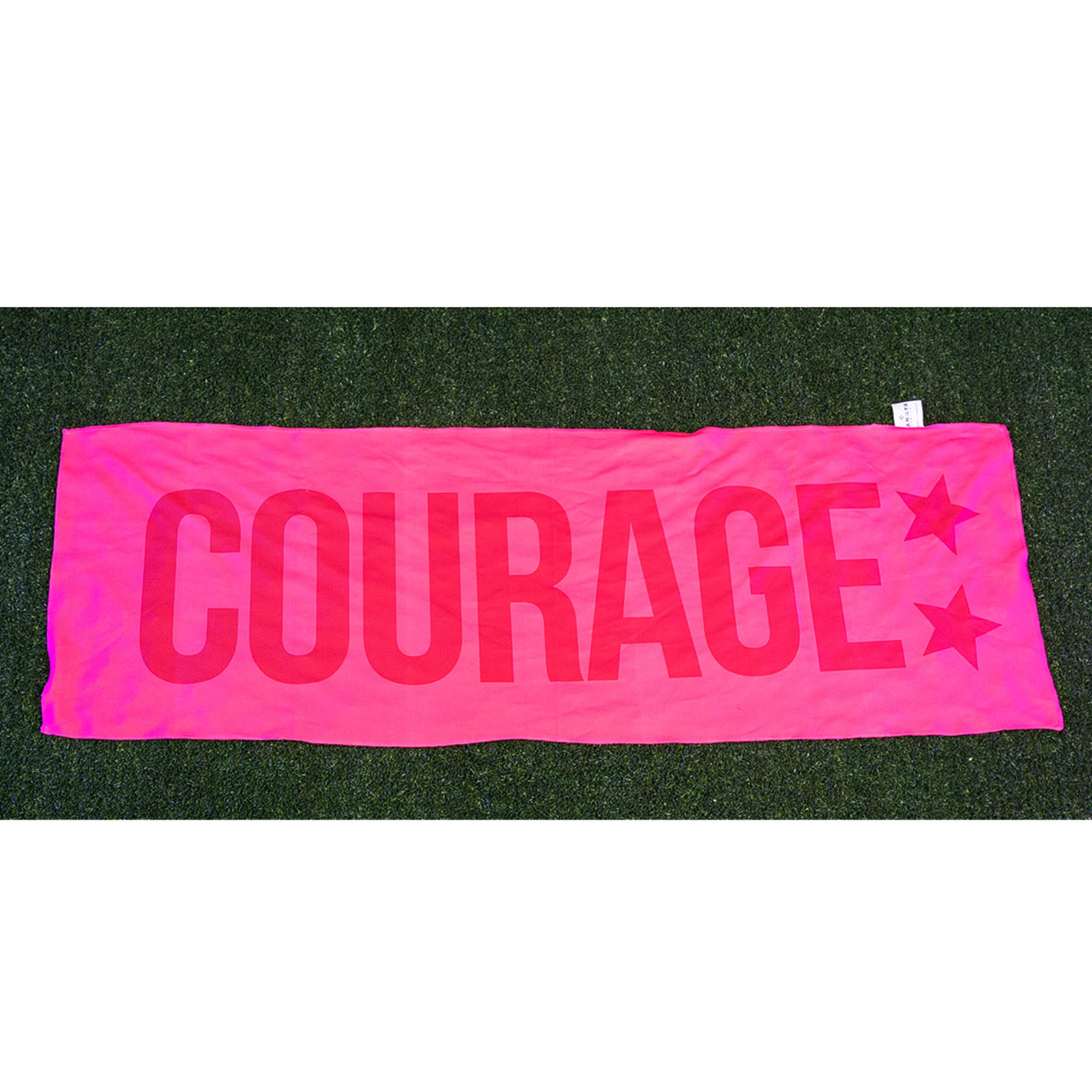 A pink cooling towel with the word 'COURAGE' written in bold letters, placed on a grassy surface.