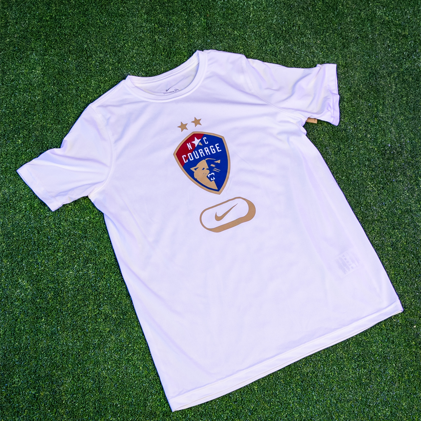 White Tee with a Courage Logo on the front and a gold nike logo.
